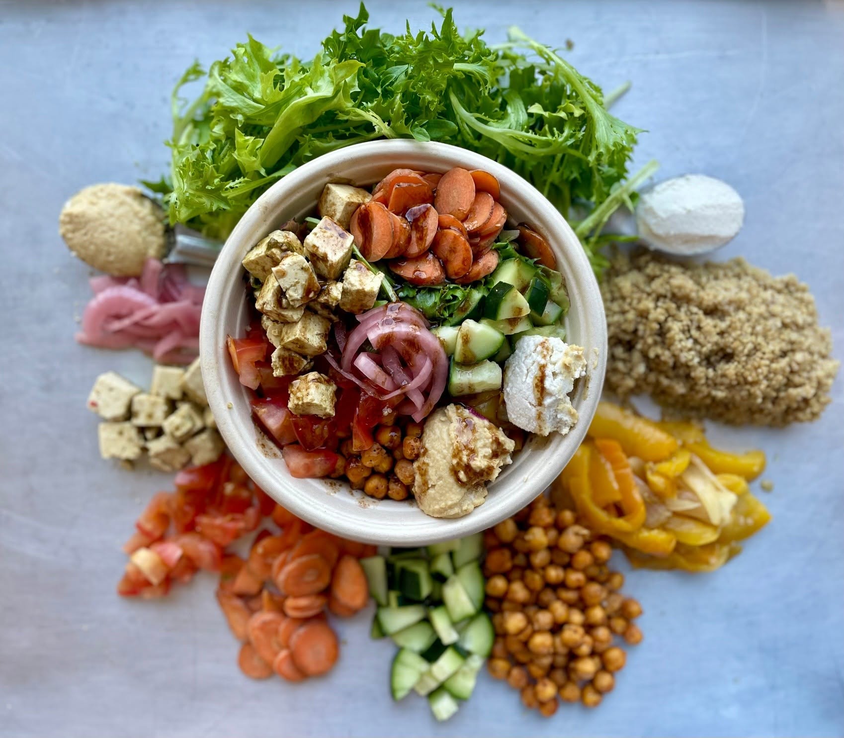 A colorful prepared bowl with fresh vegetables, tofu, and hummus